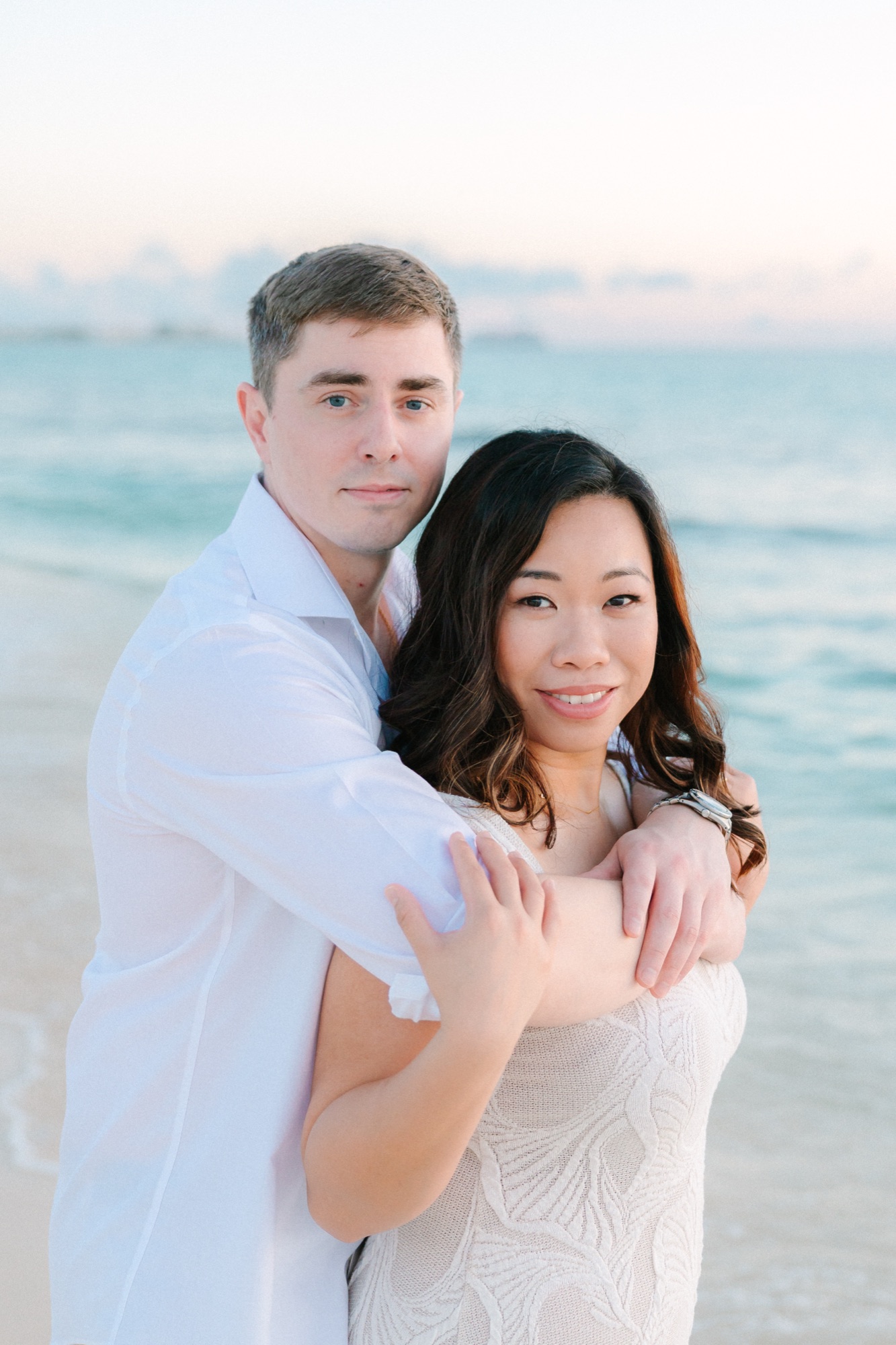 Alex and Monette embracing on the beach in Grand Cayman at sunset, the turquoise sea behind them